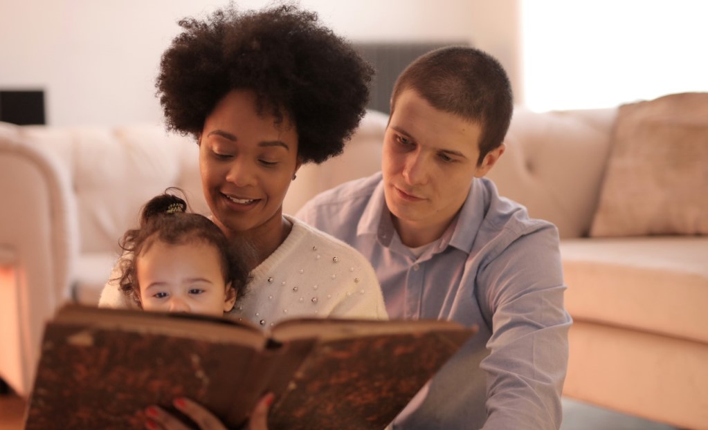 Family siting on floor with child on mother's lap looking at a bookReading to Your Kids Offers Many Benefits