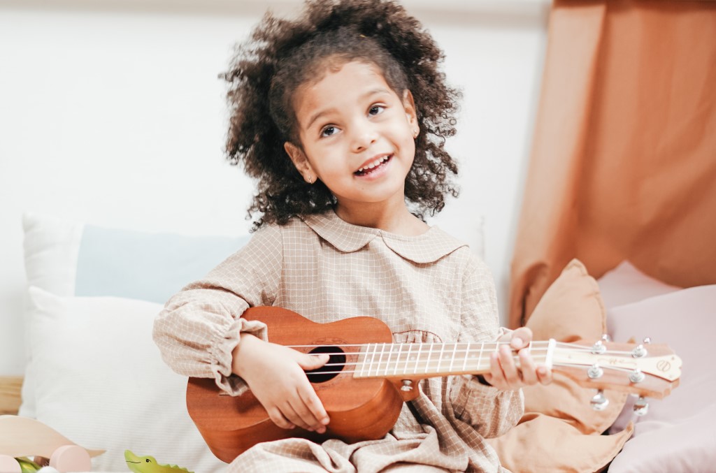 the-benefits-of-music-for-kids-blue-rose-foundation Cute little smiling girl strumming ukulele - the benefits of music for kids is amazing